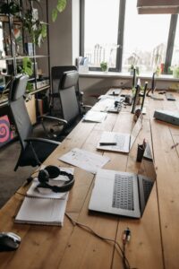 Lange houten kantoortafel met laptops, koptelefoon en planten in daglicht